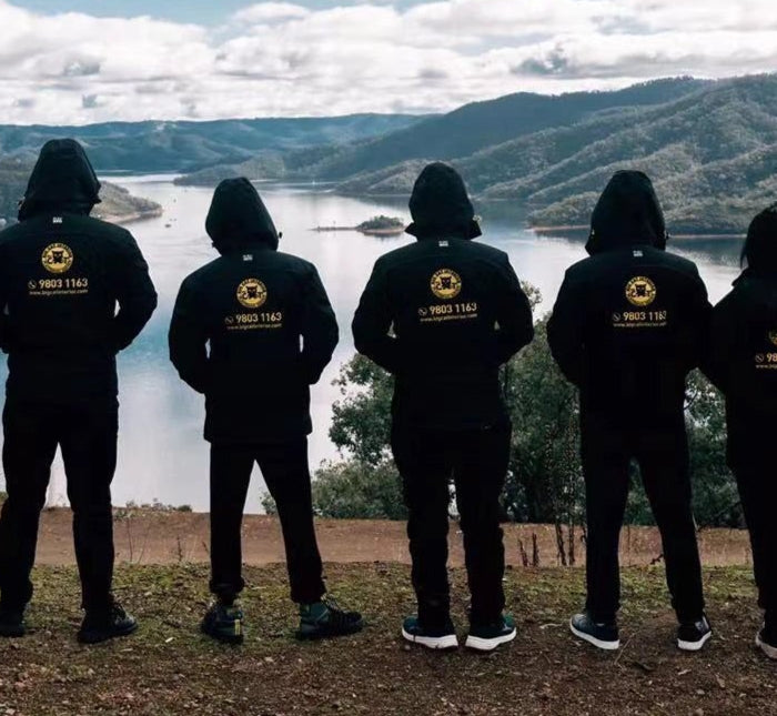 **Alt text:**
A team wearing matching custom black hoodies with gold logos stands side by side, overlooking a scenic mountain and lake view. The branded hoodies were created by My Uniform Shop, showcasing our high-quality personalised apparel for clubs, teams, and group events across Australia. Perfect for building unity, visibility, and team spirit.