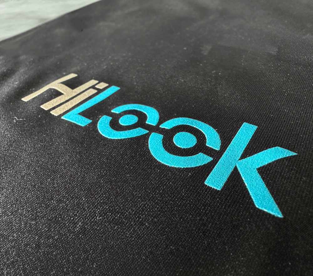 Close-up of the HiLook logo in beige and cyan printed on black fabric, with the double "o" styled as interconnected circles.