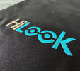 Close-up of the HiLook logo in beige and cyan printed on black fabric, with the double "o" styled as interconnected circles.