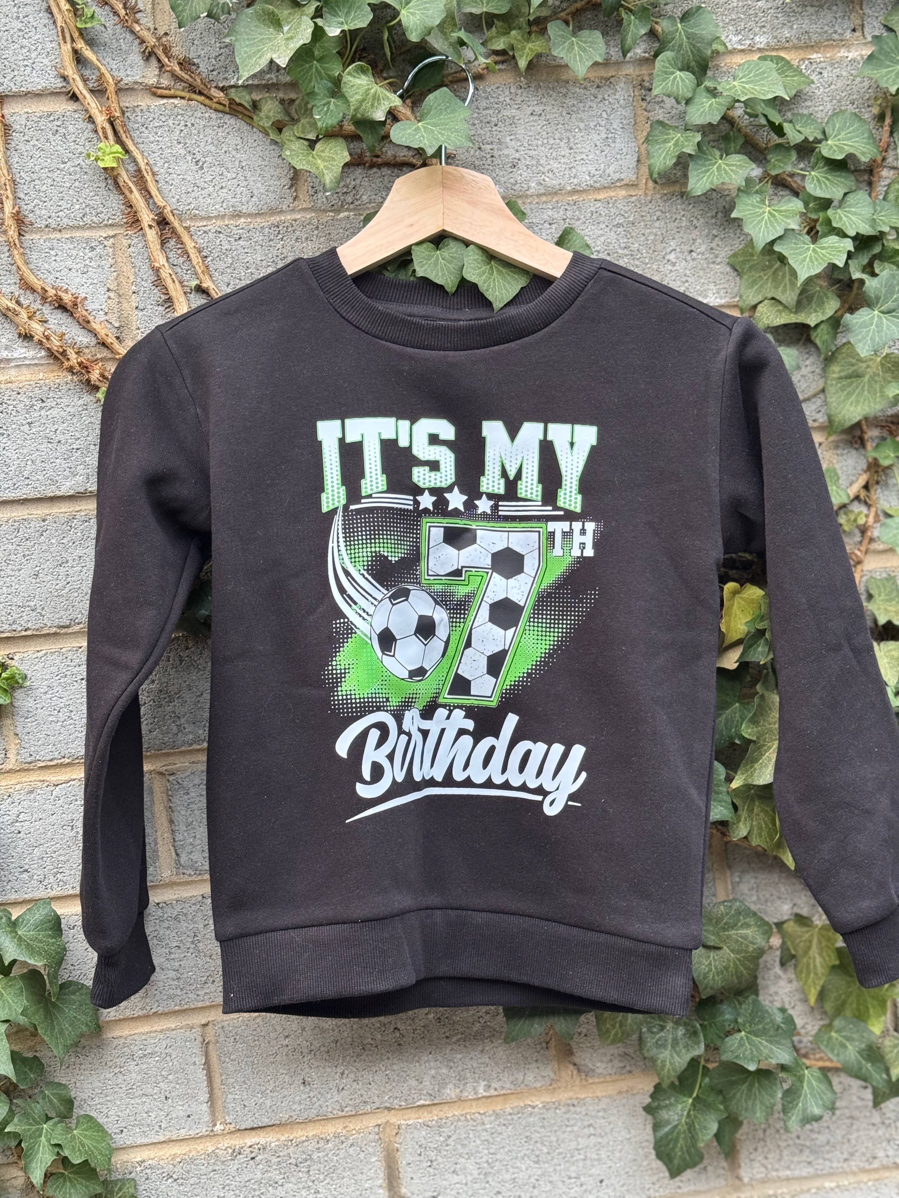 Black birthday jumper on a hanger with a green and white soccer design and birthday lettering.