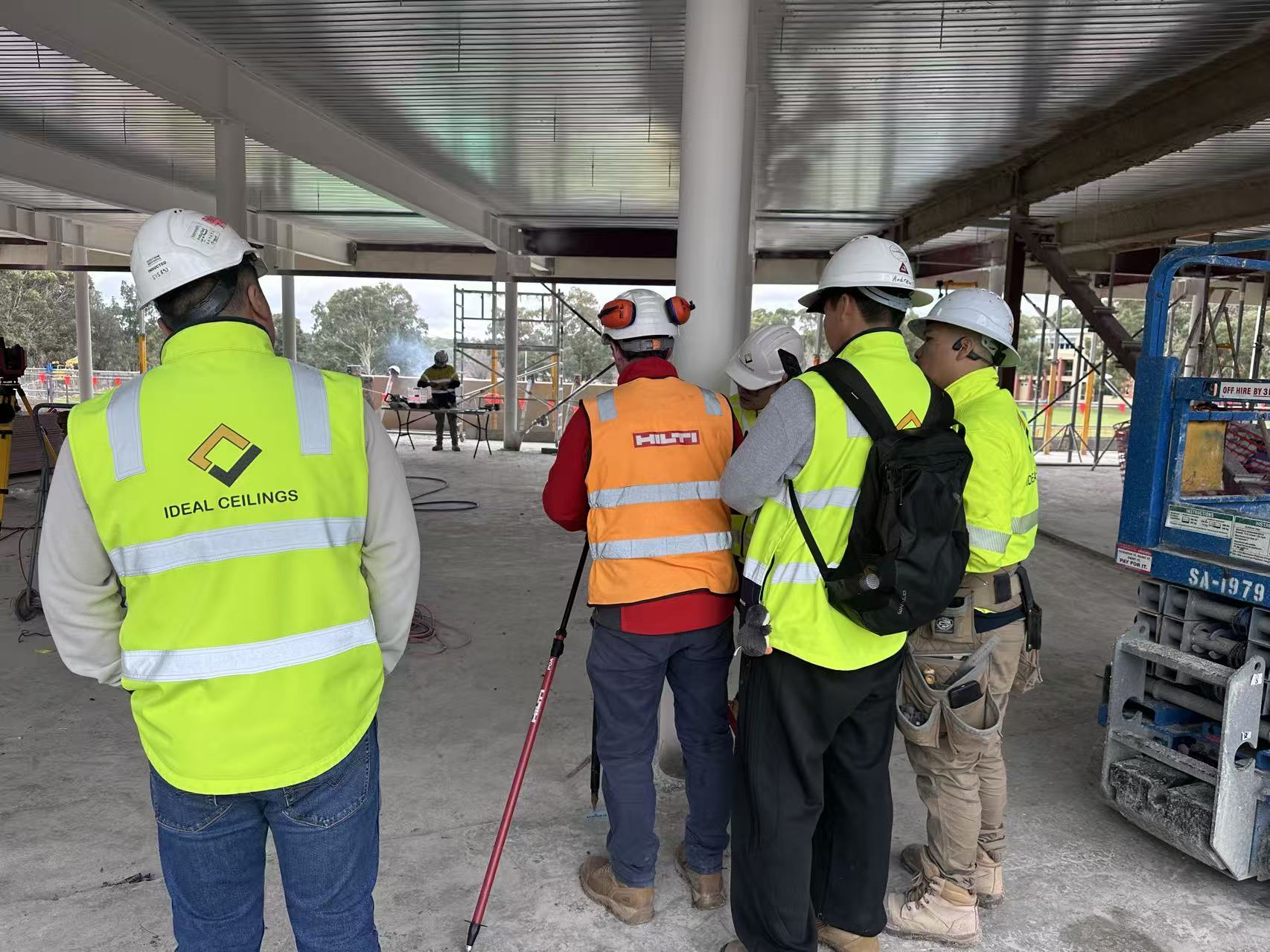 People at a construction site wearing yellow hi-vis workwear, with Ideal Ceilings branding visible on a vest.