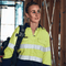 **Alt Text:** Female tradie wearing hi-vis yellow and navy work shirt with reflective tape – custom printed safety shirt with free logo included, compliant with AS/NZS standards.