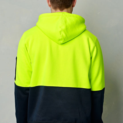 A person stands with his back to the camera. He wears a neon yellow and dark blue two-tone hoodie.