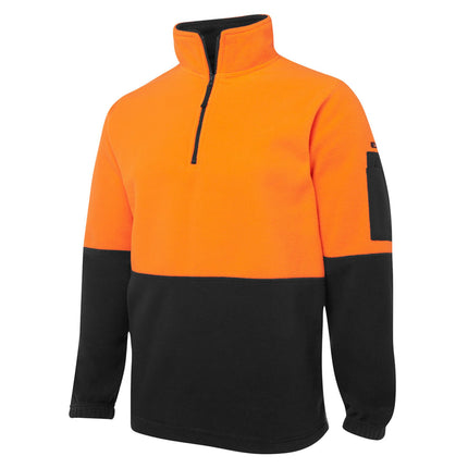 A close-up of a two-tone fleece pullover. The top is bright orange, and the bottom and sleeves are black. It has a high collar with a half zipper and a small black pocket on the left sleeve.