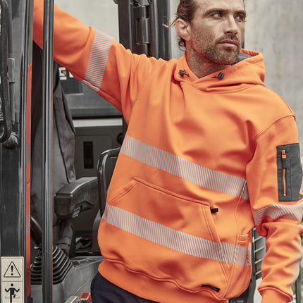 A person stands next to construction equipment. He wears a bright orange hoodie with reflective stripes and a front pocket. The hoodie has a gray zippered pocket on the left sleeve.