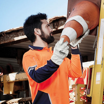 A man wearing an orange and dark blue long-sleeve polo and work gloves handles a traffic cone.