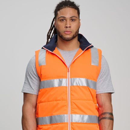 A person stands facing forward. They are wearing an orange padded vest with gray reflective stripes over a gray t-shirt. The vest has a dark blue fleece collar and hood.