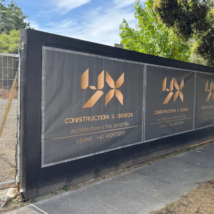 Construction company sign printed on mesh banner on a wall with trees and sky in the background