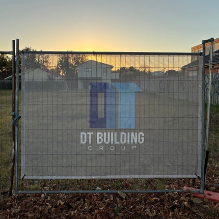 Fence mesh banner with 'DT Building Group' logo during sunset