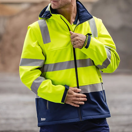 A person zipping up a two-tone work jacket. The jacket is neon yellow and dark blue with gray reflective stripes. They are also wearing a dark blue cap with a yellow logo.