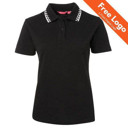 JB's Ladies Chef Polo by JB's Wear: a black short-sleeve women’s polo with a checkered collar, made from durable double pique knit. Orange banner states "Free Logo, 1 Front Digital Logo." Ideal hospitality uniform shown on white background.