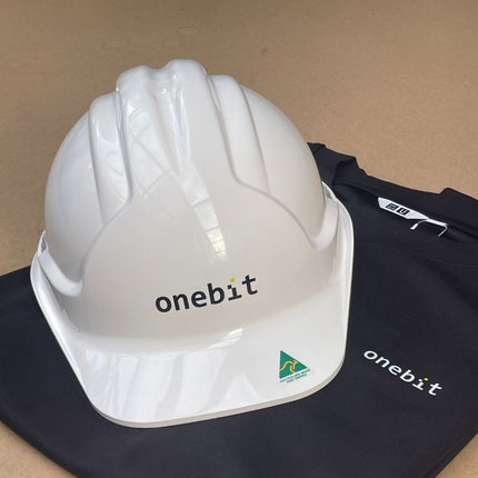 White Sureguard TUFFGARD hard hat featuring a custom "onebit" logo on the front and an Australian Made sticker on the brim, resting on a black t-shirt with a matching "onebit" logo.