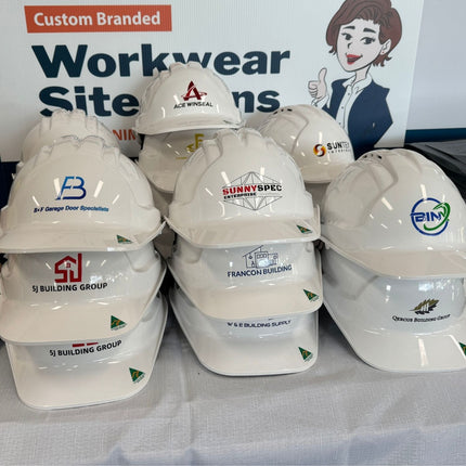 Stack of white hard hats with various logos in front of a branded backdrop.