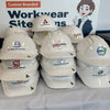 Stack of white hard hats with various logos in front of a branded backdrop.