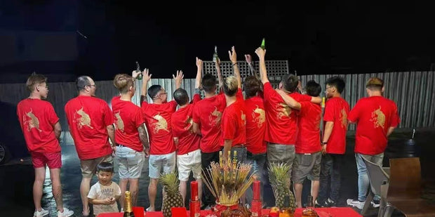 A group of friends wearing matching custom red T-shirts with a gold tiger design on the back, gathered together at a festive night celebration. The personalised shirts, designed by My Uniform Shop, highlight our ability to create custom event apparel for cultural gatherings, special occasions, and team celebrations across Australia.