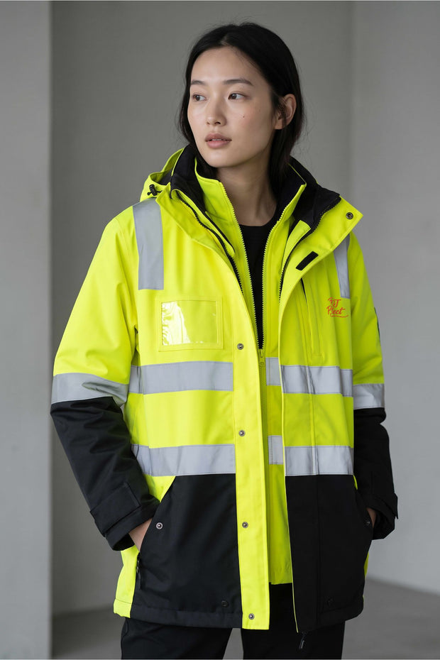A woman wearing a high-visibility safety jacket in neon yellow-green with reflective silver stripes and black lower panels, photographed against a plain gray indoor background.